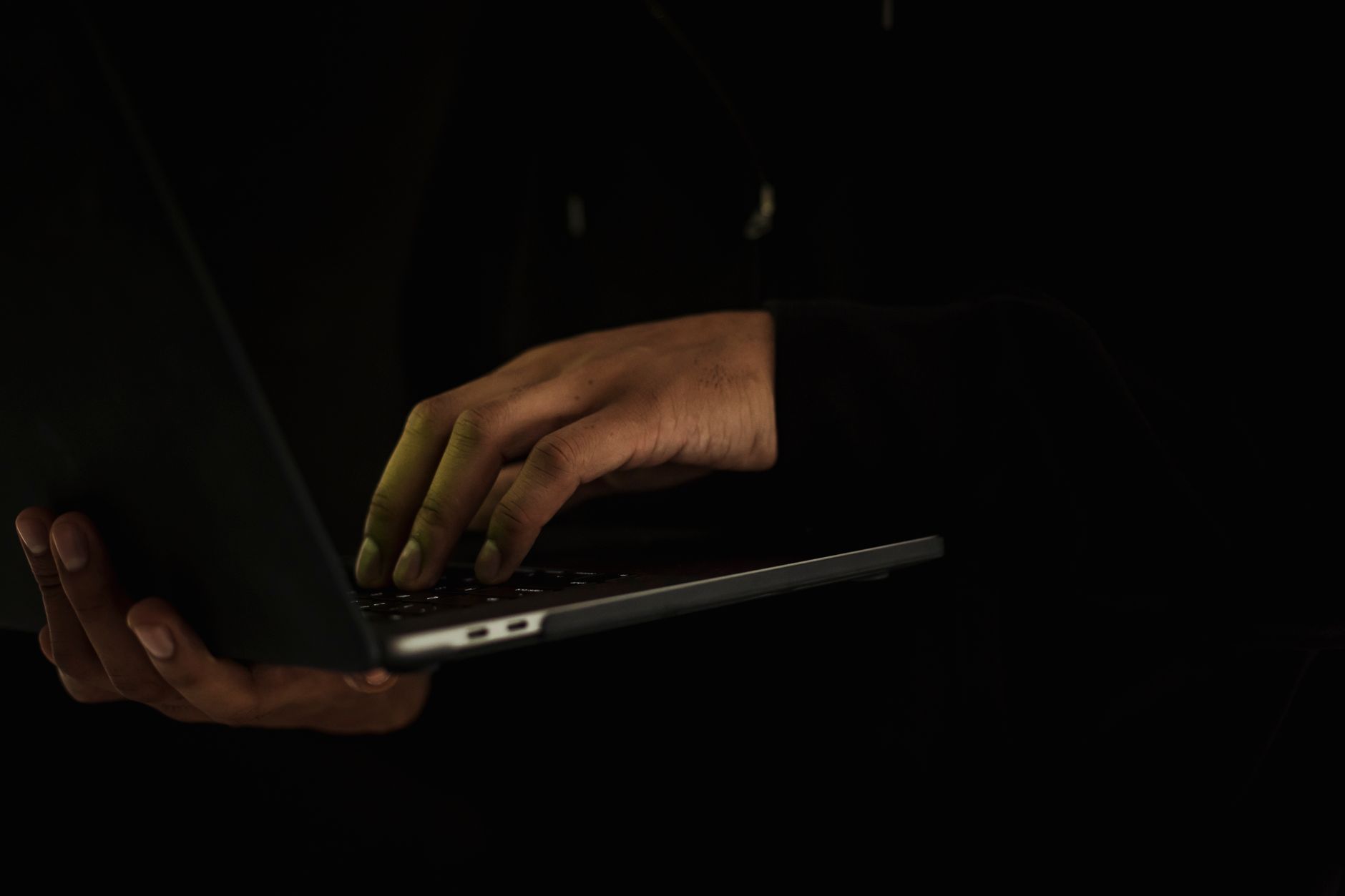 Close-up of hands typing on a laptop with a privacy filter on the screen.